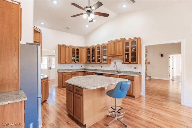 kitchen featuring high vaulted ceiling, sink, stainless steel fridge, a kitchen breakfast bar, and a center island