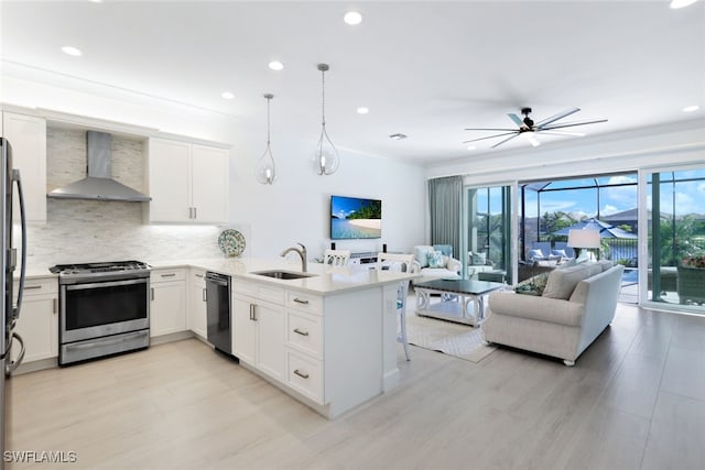 kitchen with kitchen peninsula, stainless steel appliances, wall chimney range hood, pendant lighting, and white cabinets