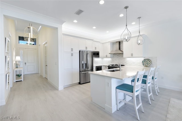 kitchen featuring stainless steel appliances, white cabinetry, pendant lighting, and wall chimney range hood