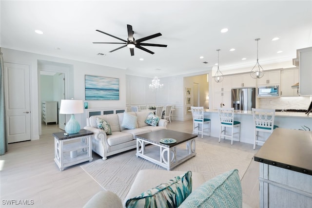 living room with ceiling fan with notable chandelier and ornamental molding