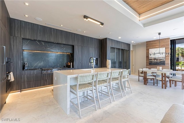 kitchen with modern cabinets, light marble finish floors, a breakfast bar, light countertops, and an island with sink
