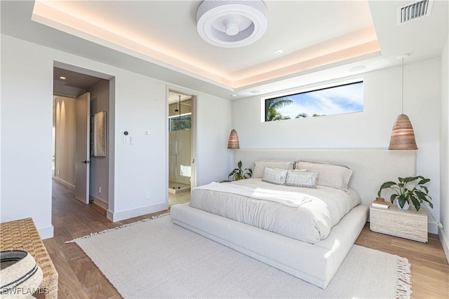 bedroom with a raised ceiling, wood finished floors, baseboards, and connected bathroom