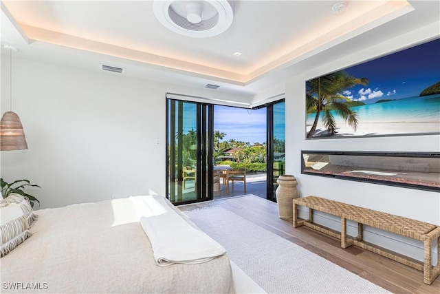bedroom with a tray ceiling, wood finished floors, and access to outside