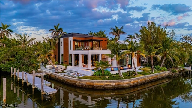 back of property with a balcony, a water view, a patio area, and an outdoor pool