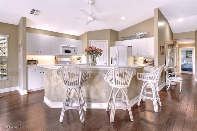 kitchen featuring white appliances, white cabinets, vaulted ceiling, ceiling fan, and a breakfast bar area