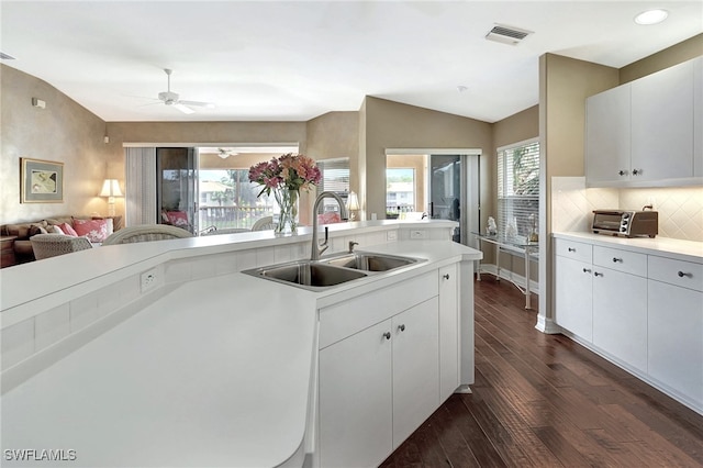 kitchen featuring backsplash, vaulted ceiling, dark wood-type flooring, sink, and white cabinetry