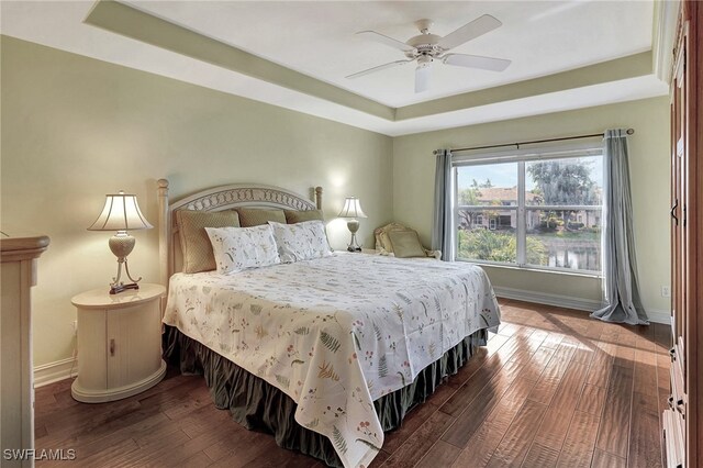 bedroom with wood-type flooring, a tray ceiling, and ceiling fan