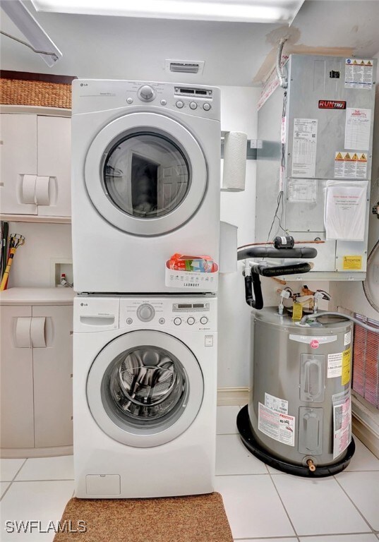 laundry area featuring cabinets, stacked washing maching and dryer, water heater, heating unit, and light tile patterned floors