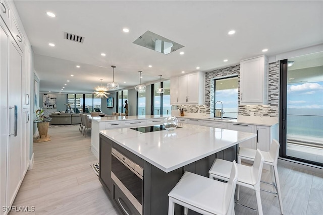 kitchen with pendant lighting, white cabinets, a kitchen breakfast bar, a spacious island, and tasteful backsplash