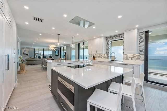 kitchen featuring a large island with sink, white cabinets, hanging light fixtures, tasteful backsplash, and a breakfast bar area