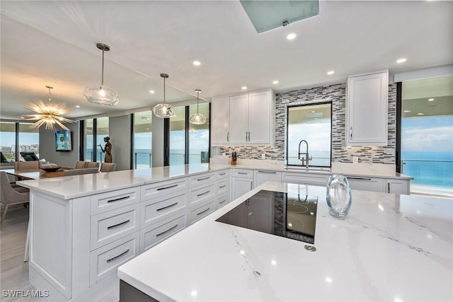 kitchen featuring white cabinets, black electric stovetop, decorative light fixtures, and sink