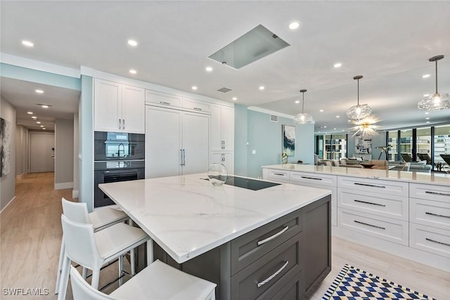 kitchen featuring a breakfast bar, white cabinets, black electric stovetop, a spacious island, and decorative light fixtures