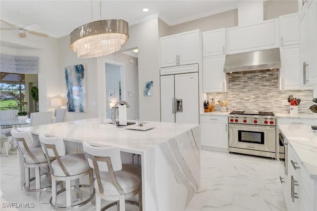 kitchen with range hood, pendant lighting, high quality appliances, a center island with sink, and white cabinets