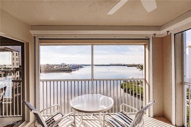 sunroom featuring ceiling fan and a water view