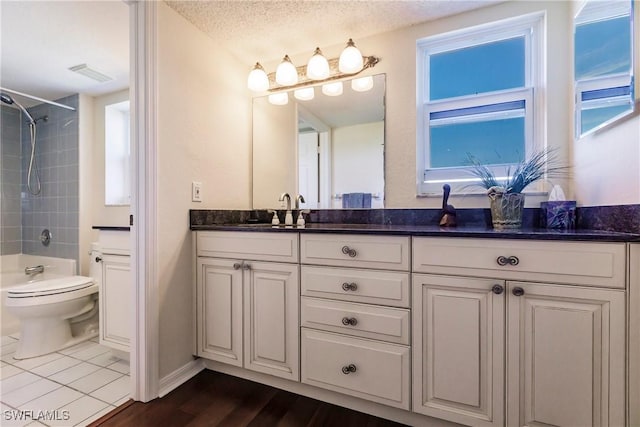 full bathroom featuring vanity, a textured ceiling, tiled shower / bath combo, hardwood / wood-style flooring, and toilet