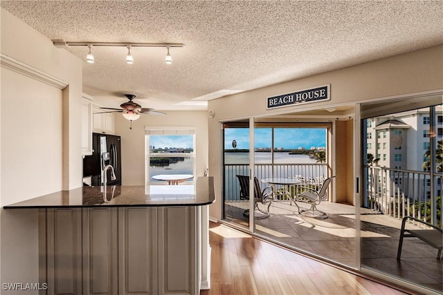 kitchen featuring light wood-type flooring, black fridge, a textured ceiling, ceiling fan, and white cabinetry