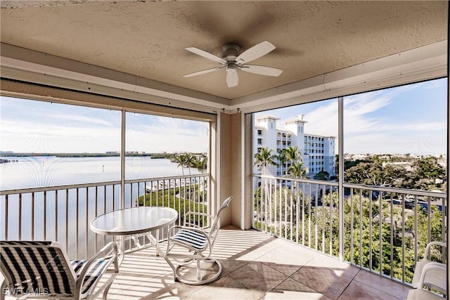 sunroom with ceiling fan and a water view