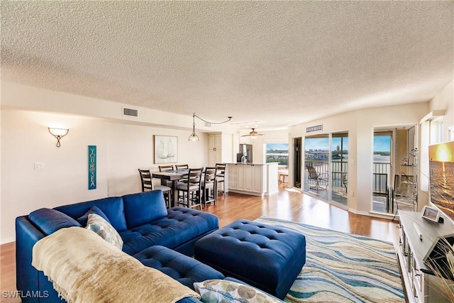 living room featuring a textured ceiling, light hardwood / wood-style flooring, and ceiling fan