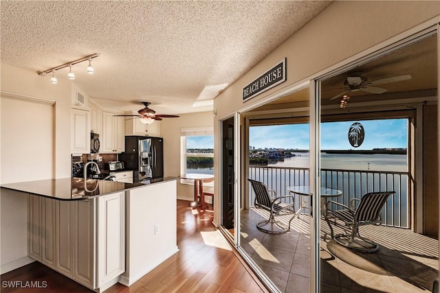 kitchen with white cabinets, stainless steel fridge with ice dispenser, a water view, and kitchen peninsula