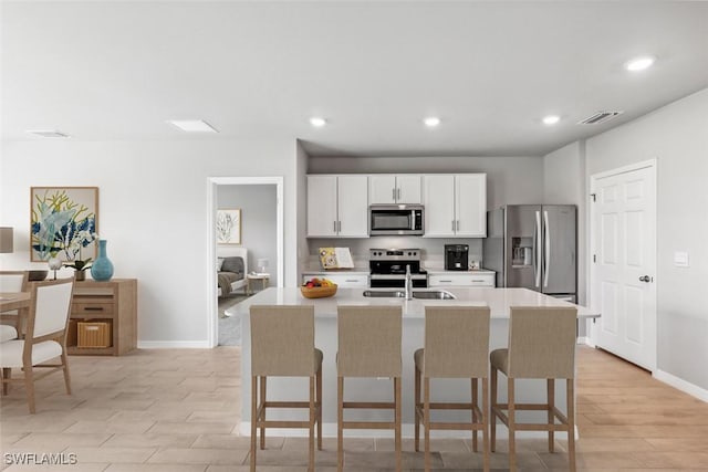 kitchen featuring a center island with sink, a kitchen breakfast bar, white cabinetry, and stainless steel appliances