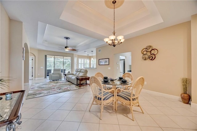 tiled dining space with ceiling fan with notable chandelier and a raised ceiling