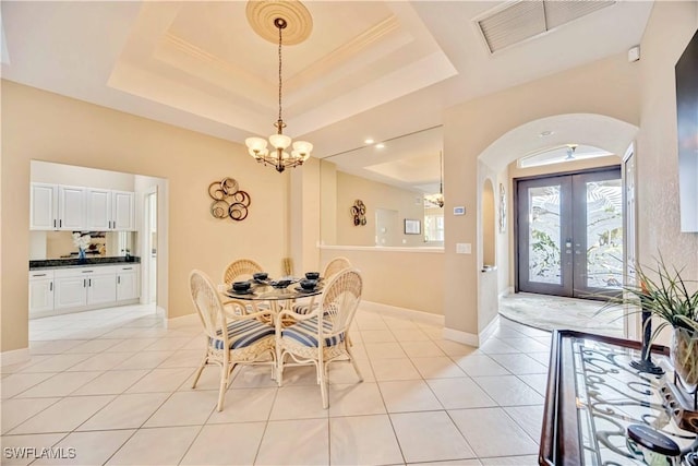 tiled dining area with an inviting chandelier, a tray ceiling, and french doors