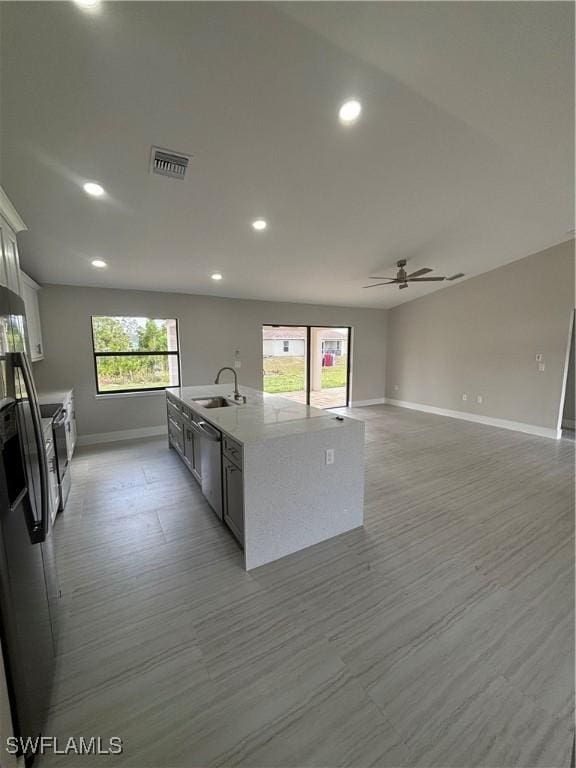 kitchen with white cabinets, ceiling fan, sink, dishwasher, and an island with sink