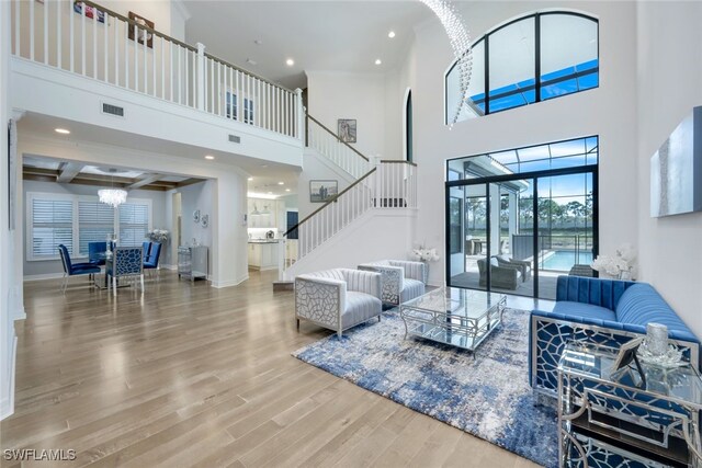 living room with coffered ceiling, a high ceiling, beamed ceiling, a notable chandelier, and wood-type flooring