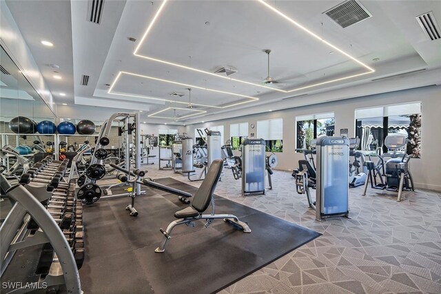 workout area with ceiling fan and a tray ceiling