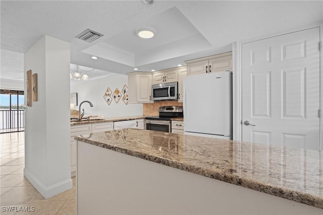 kitchen with light stone countertops, stainless steel appliances, sink, a raised ceiling, and light tile patterned floors