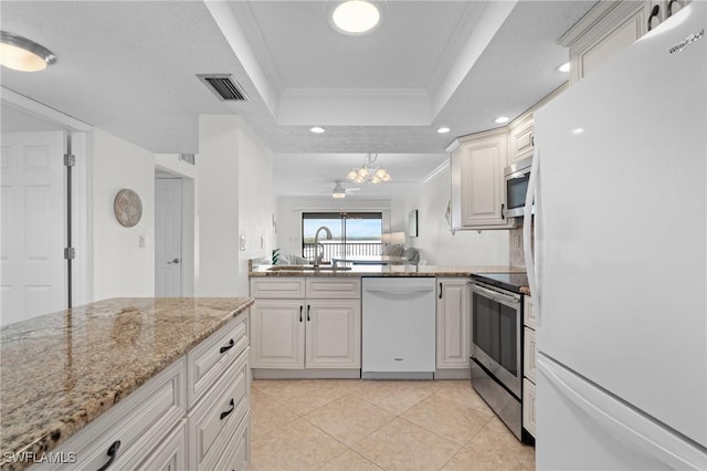 kitchen with light stone countertops, appliances with stainless steel finishes, white cabinetry, sink, and a raised ceiling