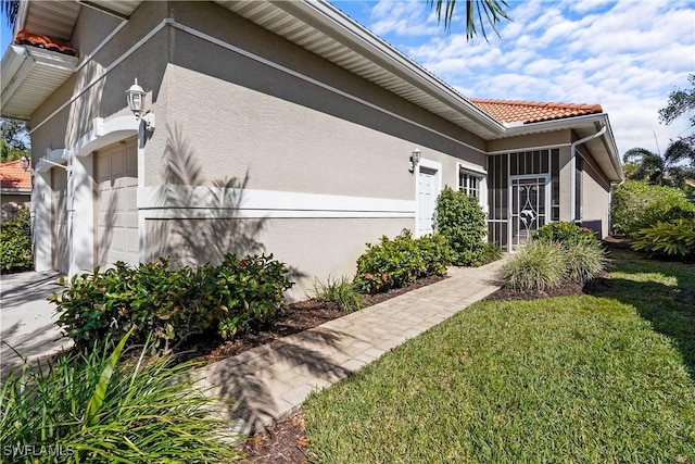 view of side of home with a garage, a tiled roof, a lawn, and stucco siding