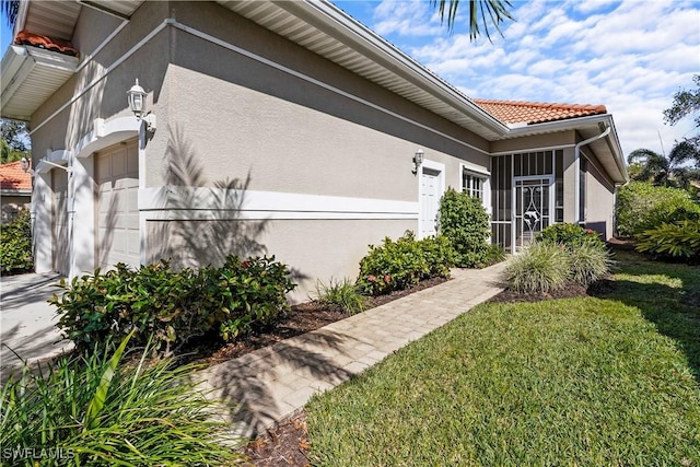 view of side of home featuring stucco siding, a lawn, a tile roof, and an attached garage