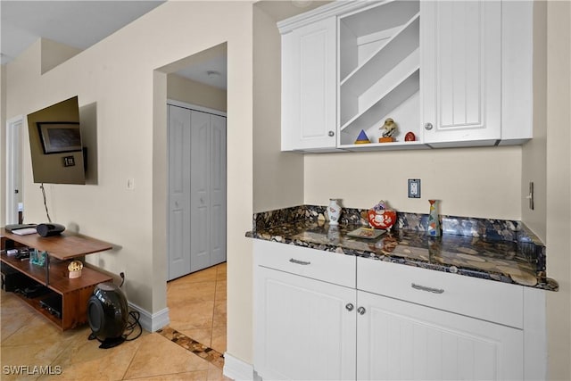 kitchen with light tile patterned floors, baseboards, dark stone countertops, white cabinetry, and open shelves