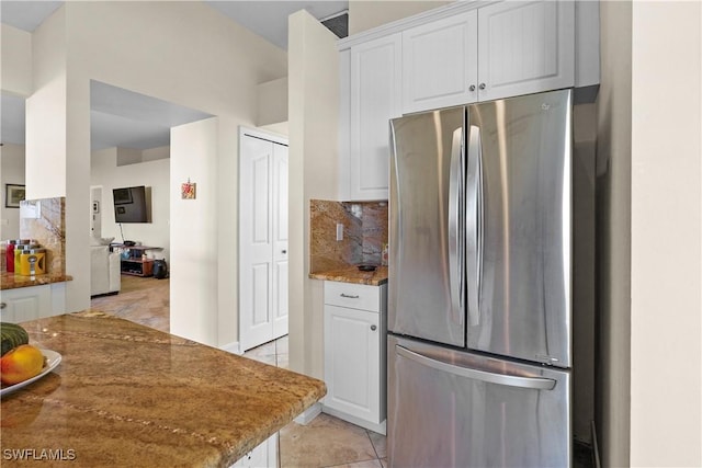 kitchen featuring freestanding refrigerator, white cabinets, stone counters, and decorative backsplash