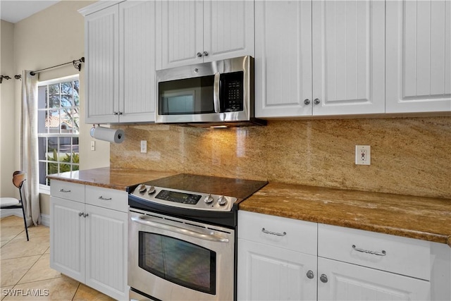 kitchen with light tile patterned floors, backsplash, appliances with stainless steel finishes, white cabinets, and dark stone counters