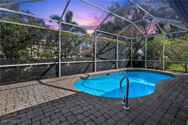 pool at dusk featuring an outdoor pool, a patio area, and a lanai