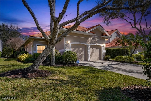 mediterranean / spanish home with an attached garage, driveway, a yard, stucco siding, and a tiled roof