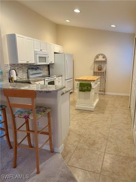 kitchen featuring light stone countertops, a kitchen bar, kitchen peninsula, white appliances, and sink