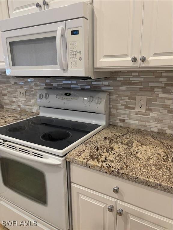 kitchen with tasteful backsplash, light stone countertops, white cabinets, and white appliances