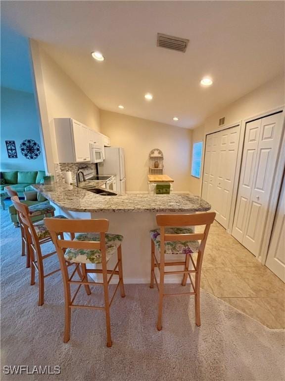 kitchen featuring white appliances, white cabinets, sink, light stone counters, and kitchen peninsula