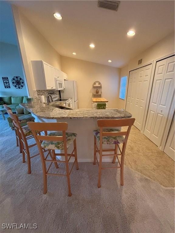 kitchen with a breakfast bar, white appliances, kitchen peninsula, tasteful backsplash, and white cabinetry