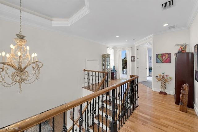 corridor with a raised ceiling, crown molding, light hardwood / wood-style flooring, and a chandelier