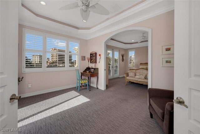 living area with a raised ceiling, ceiling fan, carpet, and ornamental molding