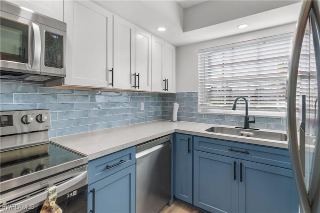 kitchen with blue cabinetry, sink, decorative backsplash, white cabinets, and appliances with stainless steel finishes