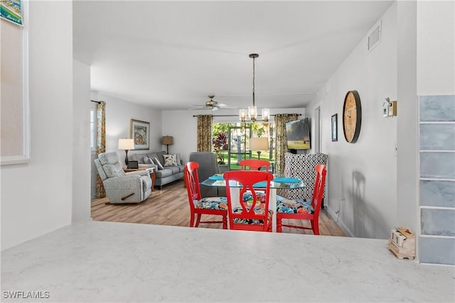 dining space featuring wood-type flooring and ceiling fan with notable chandelier