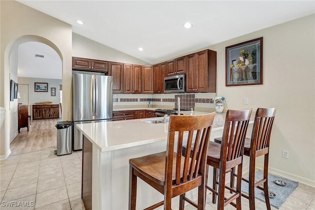 kitchen with vaulted ceiling, light tile patterned flooring, a kitchen bar, kitchen peninsula, and stainless steel appliances