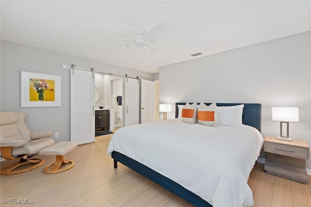 bedroom featuring a barn door, light hardwood / wood-style floors, ensuite bath, and ceiling fan