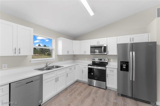 kitchen with white cabinets, stainless steel appliances, vaulted ceiling, and sink