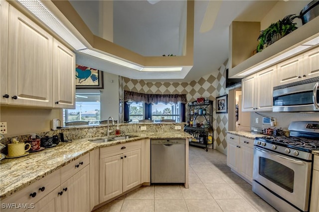 kitchen featuring light stone countertops, kitchen peninsula, stainless steel appliances, sink, and light tile patterned flooring